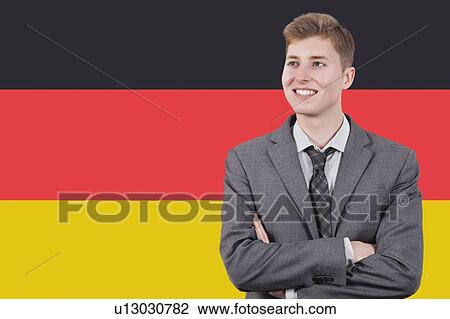 Stock Image - Young businessman with arms crossed over German flag. Fotosearch