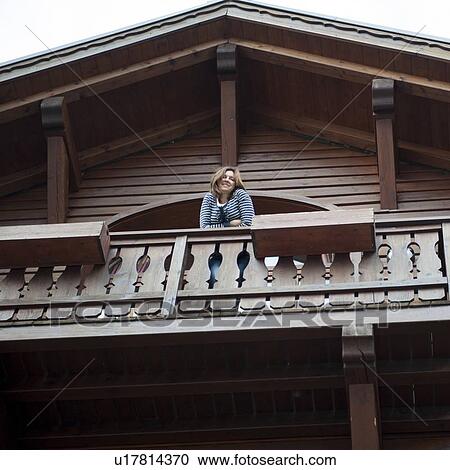 Stock Image - Low angle view of a woman leaning on the balcony of a chalet, Chamonix, Rhone-Alpes, France. Fotosearch