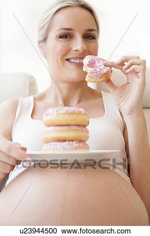 Stock Image - Pregnant woman eating doughnuts. Fotosearch