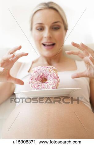 Stock Image - Pregnant woman with doughnuts. Fotosearch