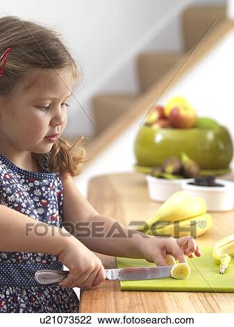 Stock Image - Young girl cutting a banana. Fotosearch
