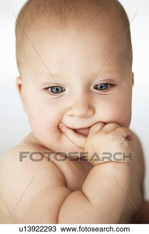 Stock Image - Baby girl holding finger to mouth. Fotosearch