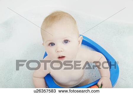 Stock Image - Baby girl sitting in seat in bath. Fotosearch