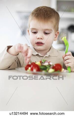 Picture - Boy picking at plate of fruit in kitchen. Fotosearch