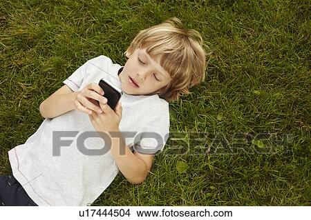Picture - Boy using cell phone in grass. Fotosearch