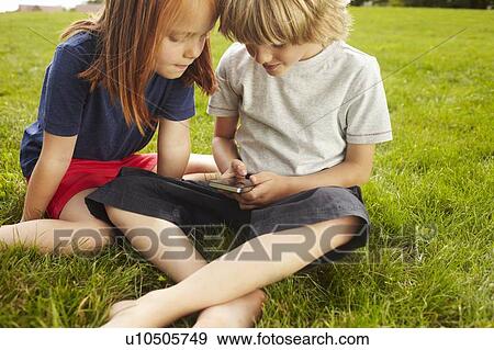 Stock Photo - Children using cell phone in grass. Fotosearch