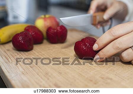 Stock Image - Close up of woman cutting fruit. Fotosearch