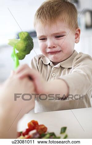 Stock Image - Crying boy refusing broccoli in kitchen. Fotosearch