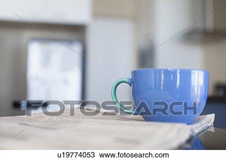 Stock Image - Cup of coffee and newspaper in kitchen. Fotosearch