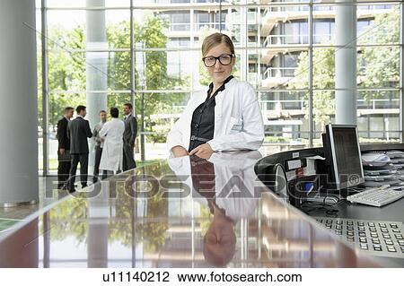Stock Image - Doctor leaning on secretarys desk. Fotosearch