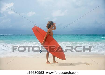 Stock Image - Man carrying surfboard on tropical beach. Fotosearch
