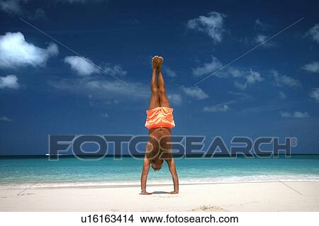Picture - Man doing handstand on tropical beach. Fotosearch