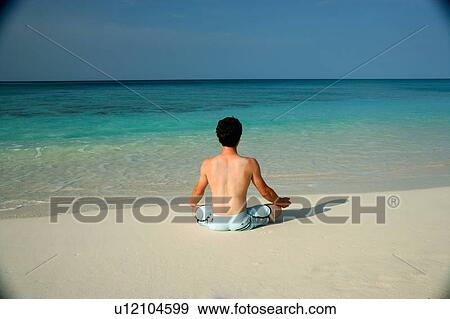 Stock Photo - Man meditating on tropical beach. Fotosearch