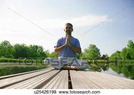 Stock Photo - Man meditating on wooden pier. Fotosearch