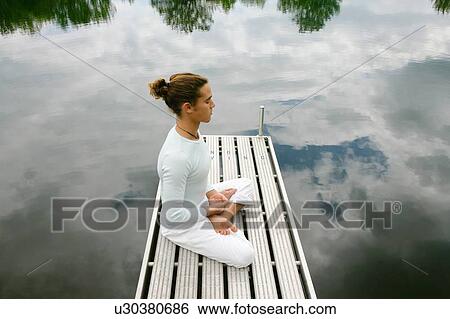 Stock Photograph - Man meditating on wooden pier. Fotosearch