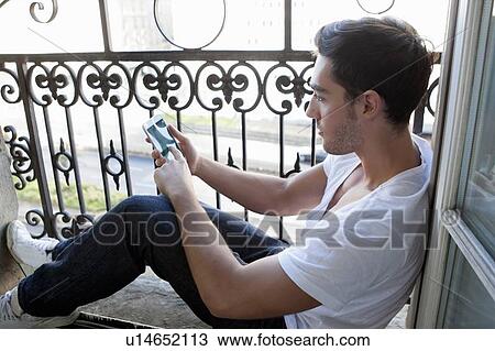 Stock Image - Man using cell phone in windowsill. Fotosearch