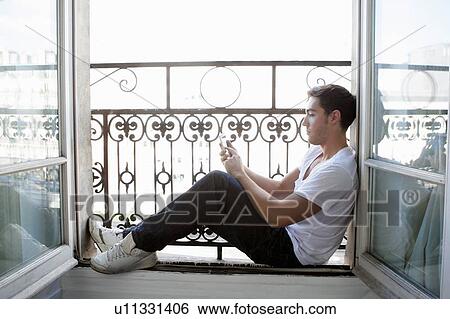 Man using cell phone in windowsill View Large Photo Image Stock Photograph - Man using cell phone in windowsill. Fotosearch