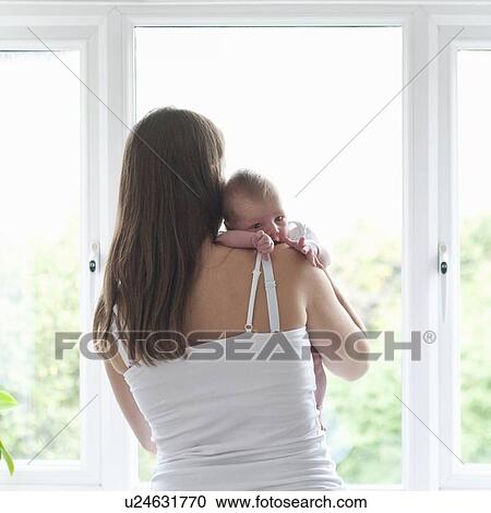 Stock Image - Mother holding infant son by window. Fotosearch