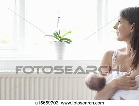 Stock Image - Mother nursing infant son by window. Fotosearch
