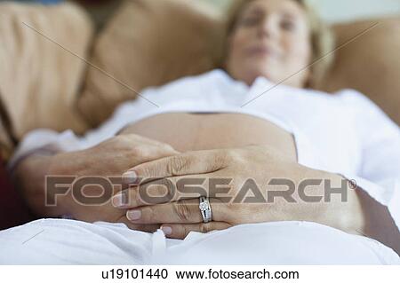 Stock Image - Pregnant woman relaxing on sofa. Fotosearch