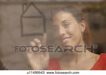 Stock Image - Smiling woman drawing on window. Fotosearch