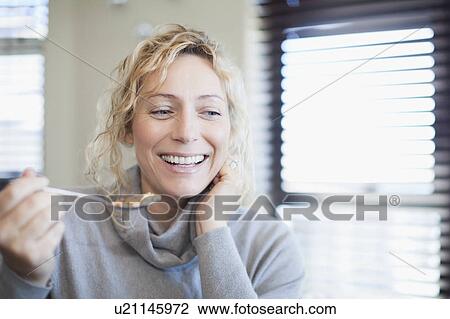 Stock Image - Smiling woman eating cereal indoors. Fotosearch