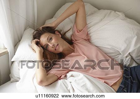 Stock Image - Smiling woman laying on bed. Fotosearch