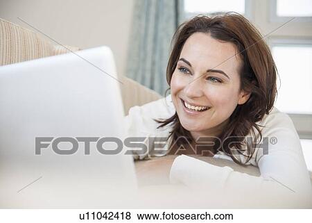 Smiling woman using laptop on sofa View Large Photo Image Stock Photo - Smiling woman using laptop on sofa. Fotosearch