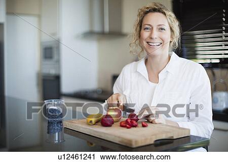 Stock Image - Woman cutting fruit in kitchen. Fotosearch