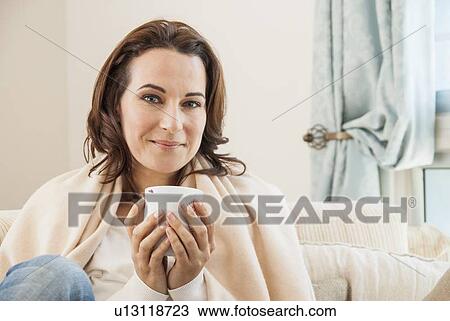 Stock Image - Woman having cup of coffee on sofa. Fotosearch