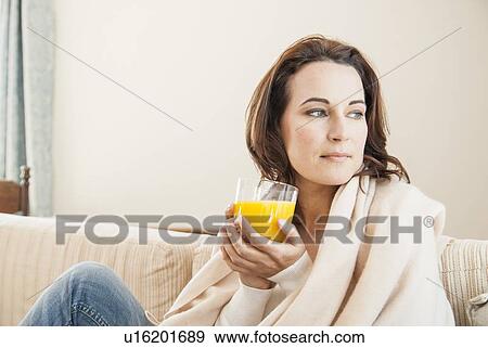 Stock Photo - Woman having cup of juice on sofa. Fotosearch