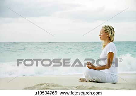 Stock Photograph - Woman meditating on tropical beach. Fotosearch