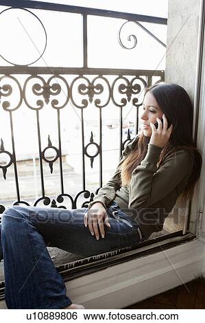 Stock Photograph - Woman on cell phone in windowsill. Fotosearch