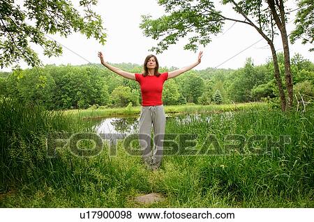 Stock Photo - Woman practicing yoga by rural lake. Fotosearch