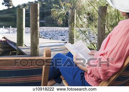 Stock Image - Woman reading in lawn chair on deck. Fotosearch
