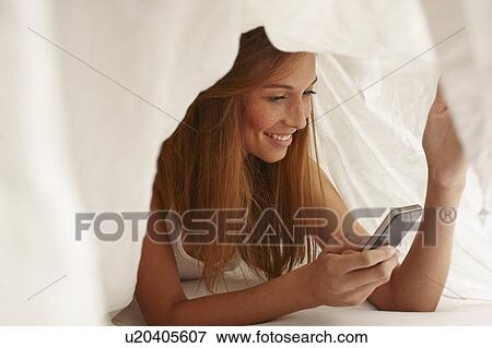 Woman using cell phone under covers View Large Photo Image Stock Photo - Woman using cell phone under covers. Fotosearch