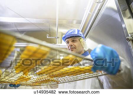 Stock Image - Worker holding tray of fish in factory. Fotosearch
