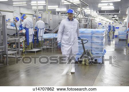 Stock Image - Worker pulling cart in factory. Fotosearch