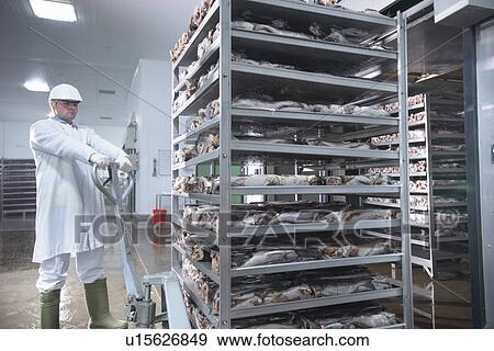 Stock Photo - Worker pulling cart in factory. Fotosearch