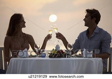 Stock Photo - Couple at table on beach, toasting. Fotosearch