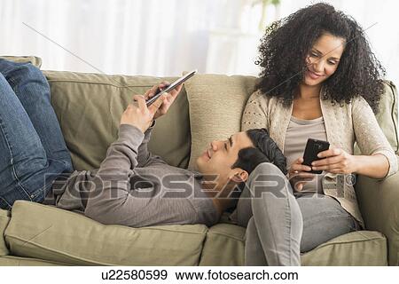 Stock Photo - Couple using digital tablet and mobile phone on sofa. Fotosearch