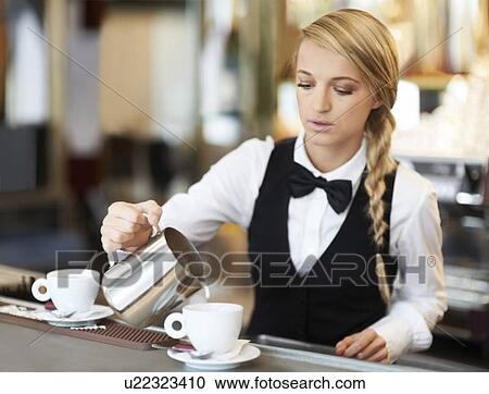 Stock Image - Female barista pouring milk into coffee cup. Fotosearch