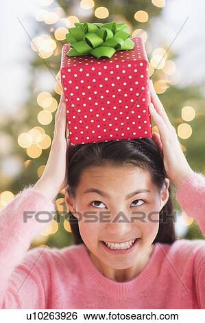 Stock Photograph - Front view of teenage girl ( 16-17 years) holding Christmas gift on head. Fotosearch