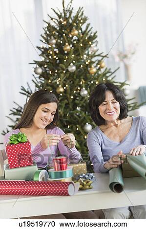 Stock Image - Grandmother and granddaughter (16-17) wrapping christmas gifts. Fotosearch