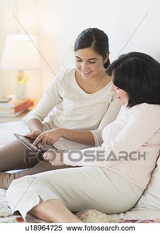 Stock Photography - Grandmother and granddaughter (16-17) lying on bed with digital tablet. Fotosearch