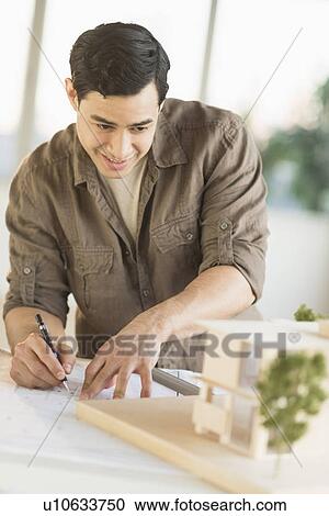 Stock Image - Male architect working with blueprint and model home. Fotosearch