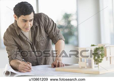 Stock Photo - Male architect working with blueprint and model home. Fotosearch