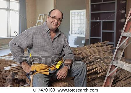 Stock Image - Man sitting on stack of planks . Fotosearch