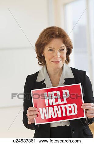 Stock Image - Portrait of businesswoman holding help wanted sign. Fotosearch