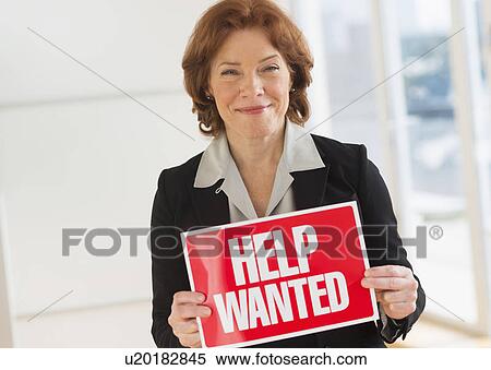 Stock Photography - Portrait of businesswoman holding help wanted sign. Fotosearch